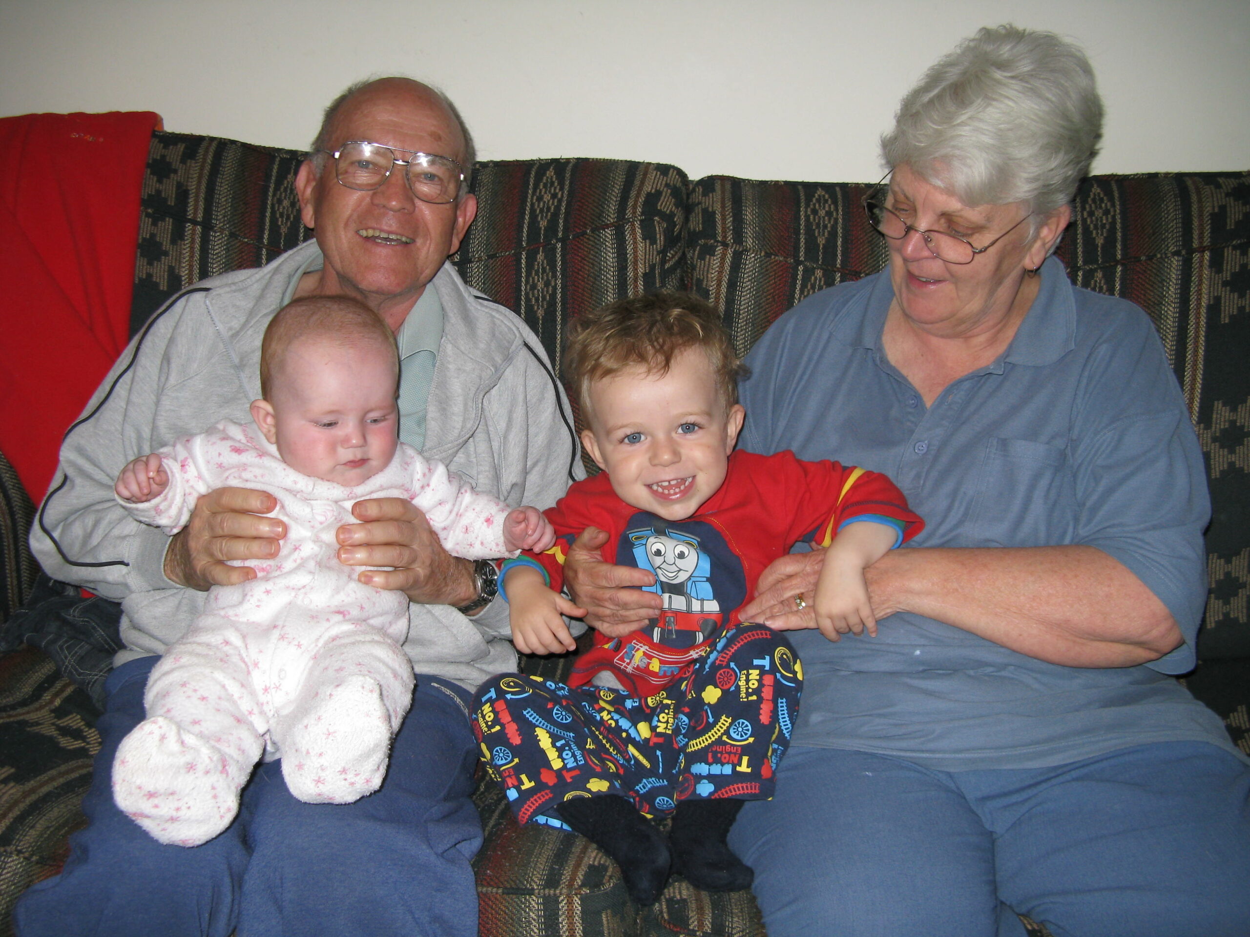 Two elderly people hold their young grandchildren sitting on a sofa.