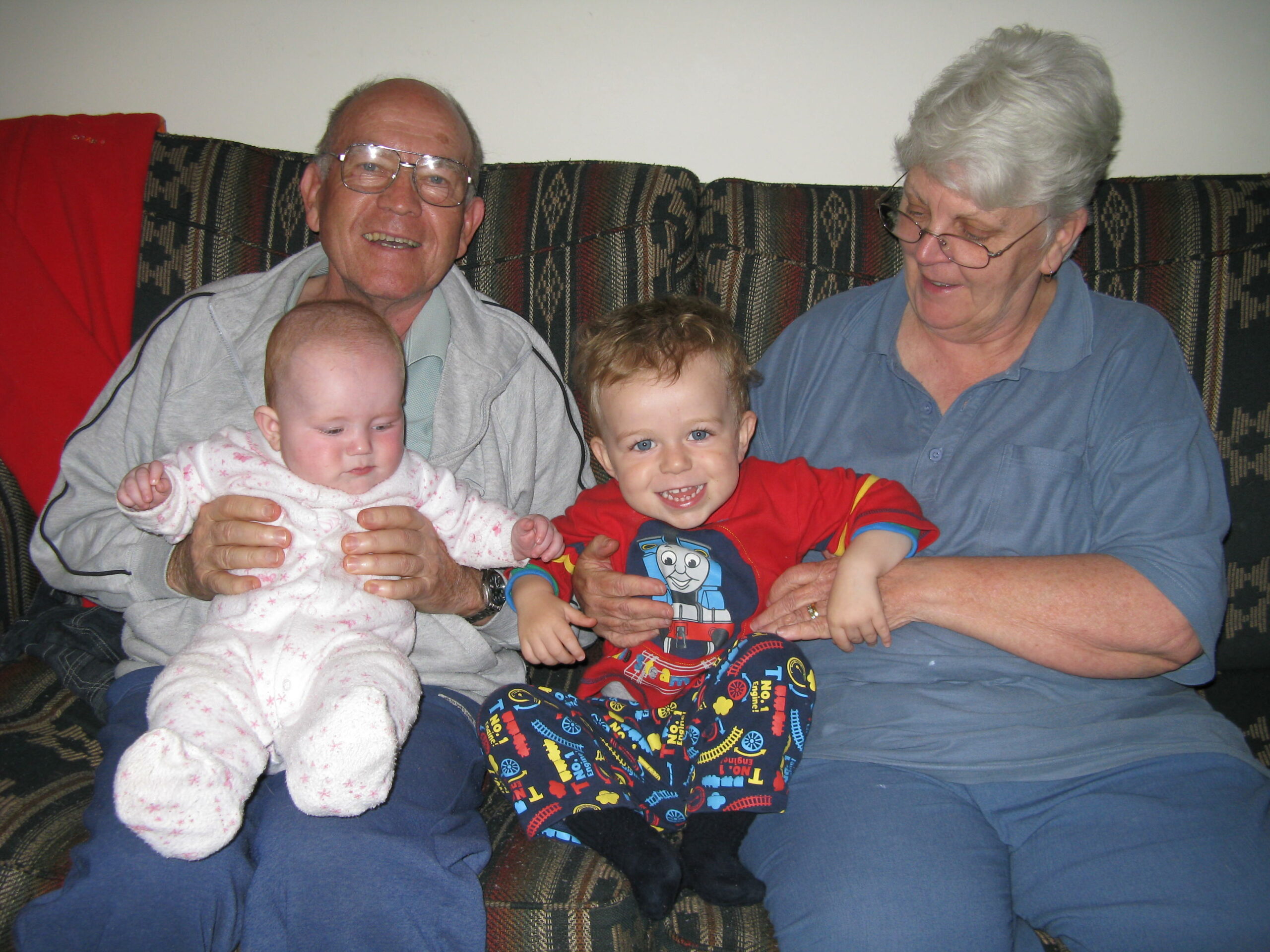 Two elderly people hold their young grandchildren sitting on a sofa.