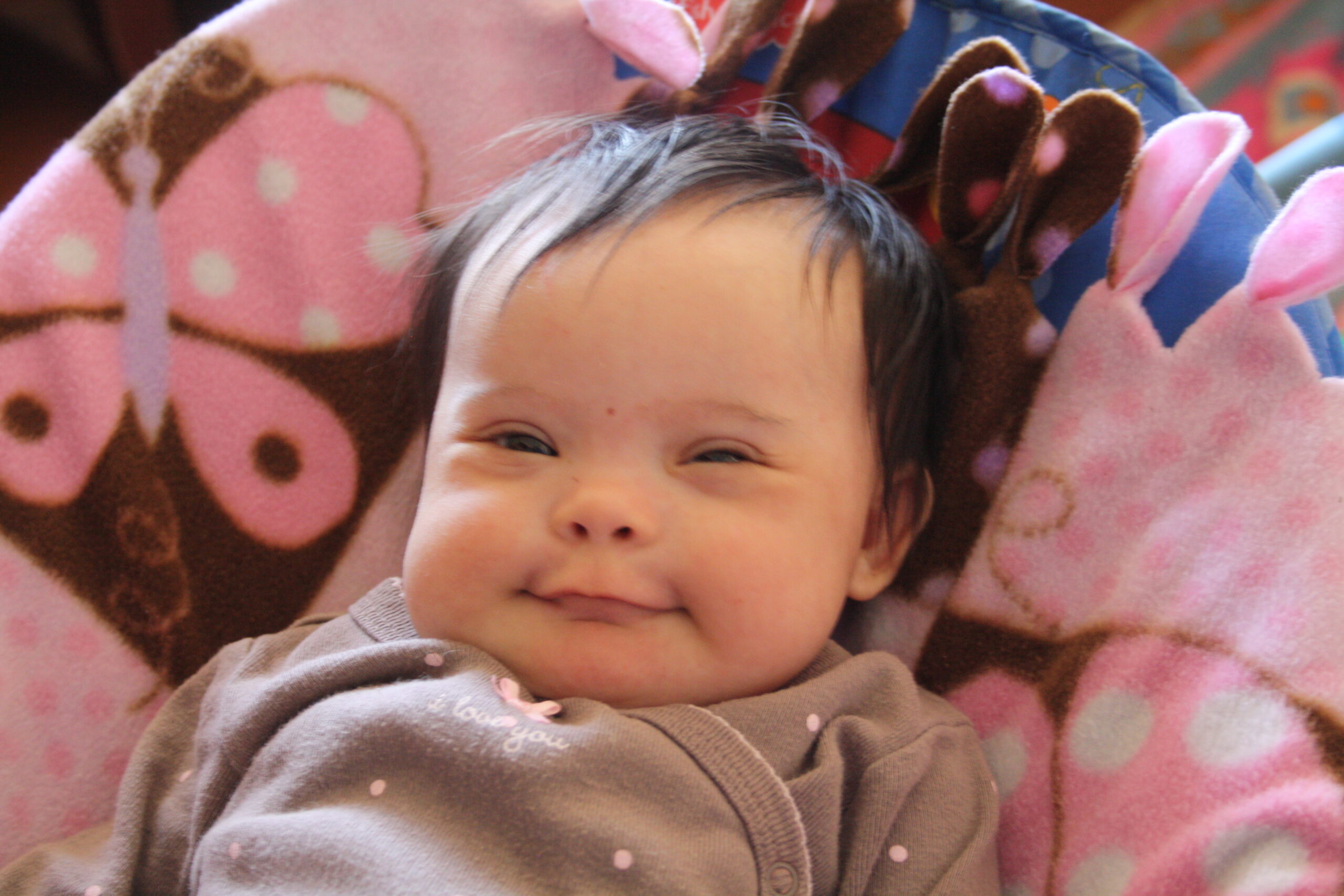 A smiling baby lays on a pink blanket.