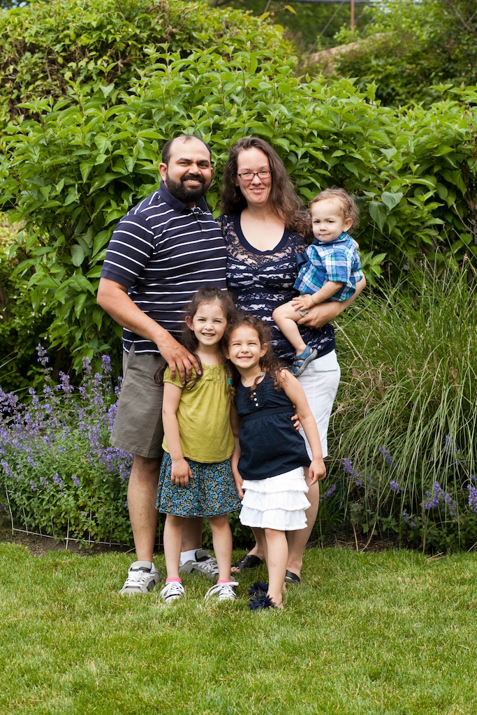 A happy family posing outside by the bushes.