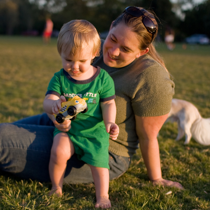 A mother sitting in the grass playing with her toddler