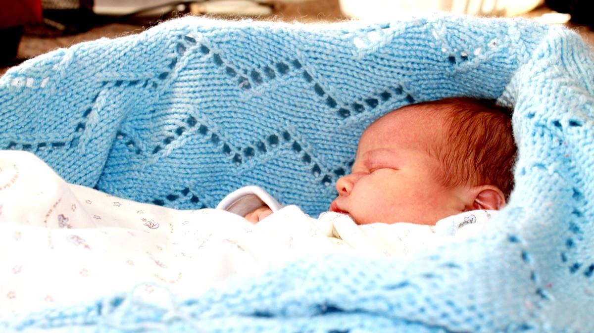 A newborn baby on a blue blanket sleeping.
