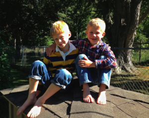 Two little boys sitting outside, one has their arm around the other