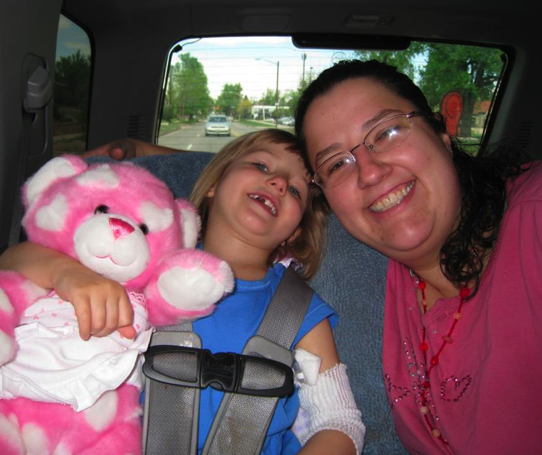 A little girl with a fuzzy pink bear and her mom in the back seat of a car