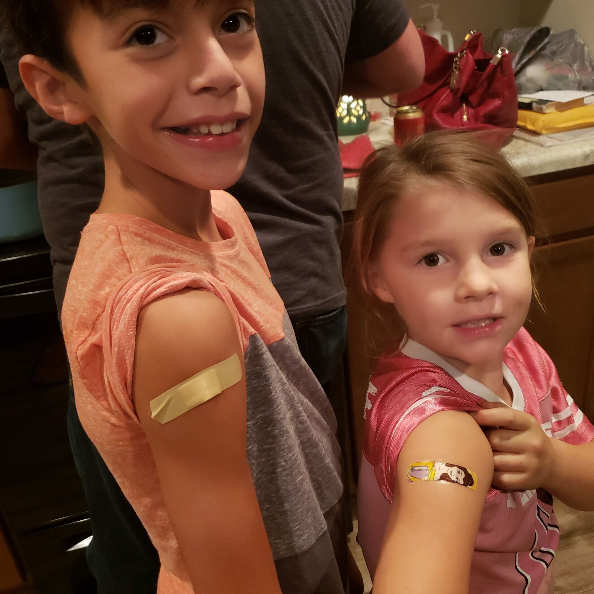 Two small children proudly show off their vaccine bandages.