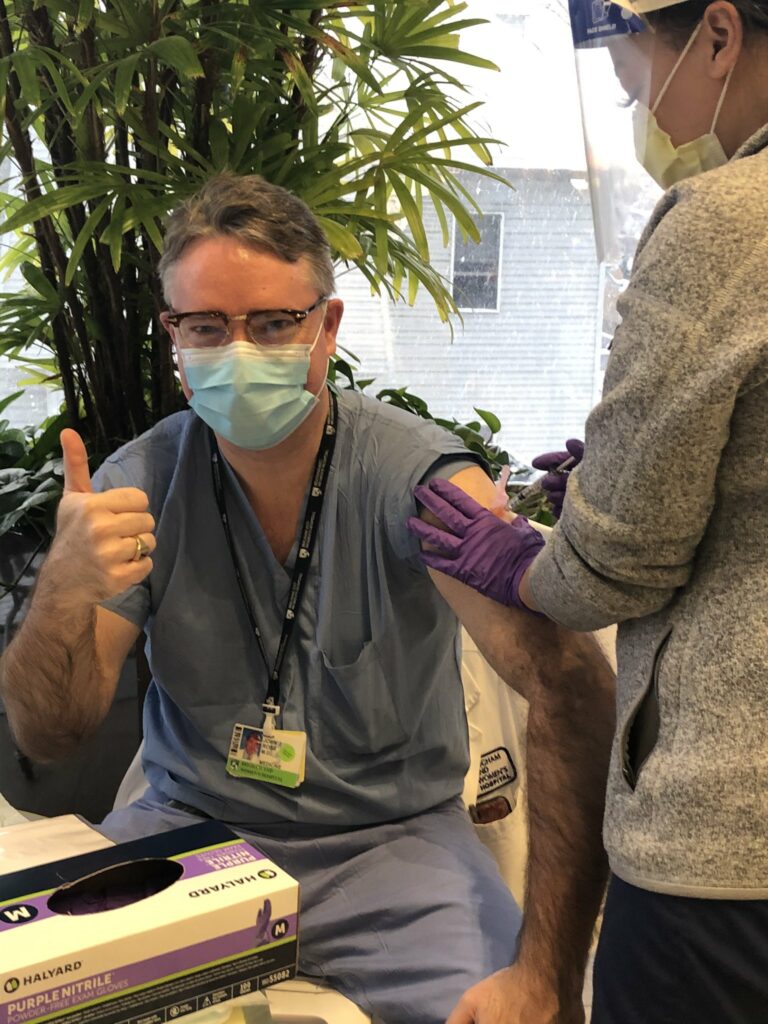 John Ross, a gray haired white man wearing glasses and a surgical mask, receives his COVID-19 vaccine. He's giving a thumbs up.