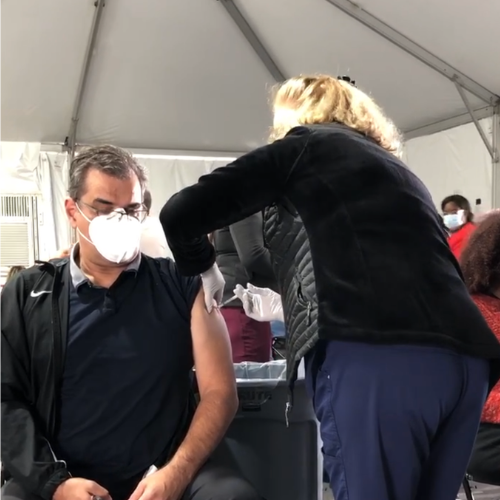 A man wearing a mask receiving a vaccine shot from a healthcare worker inside a tented facility