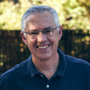 An older white man wearing a polo smiles for a photo.