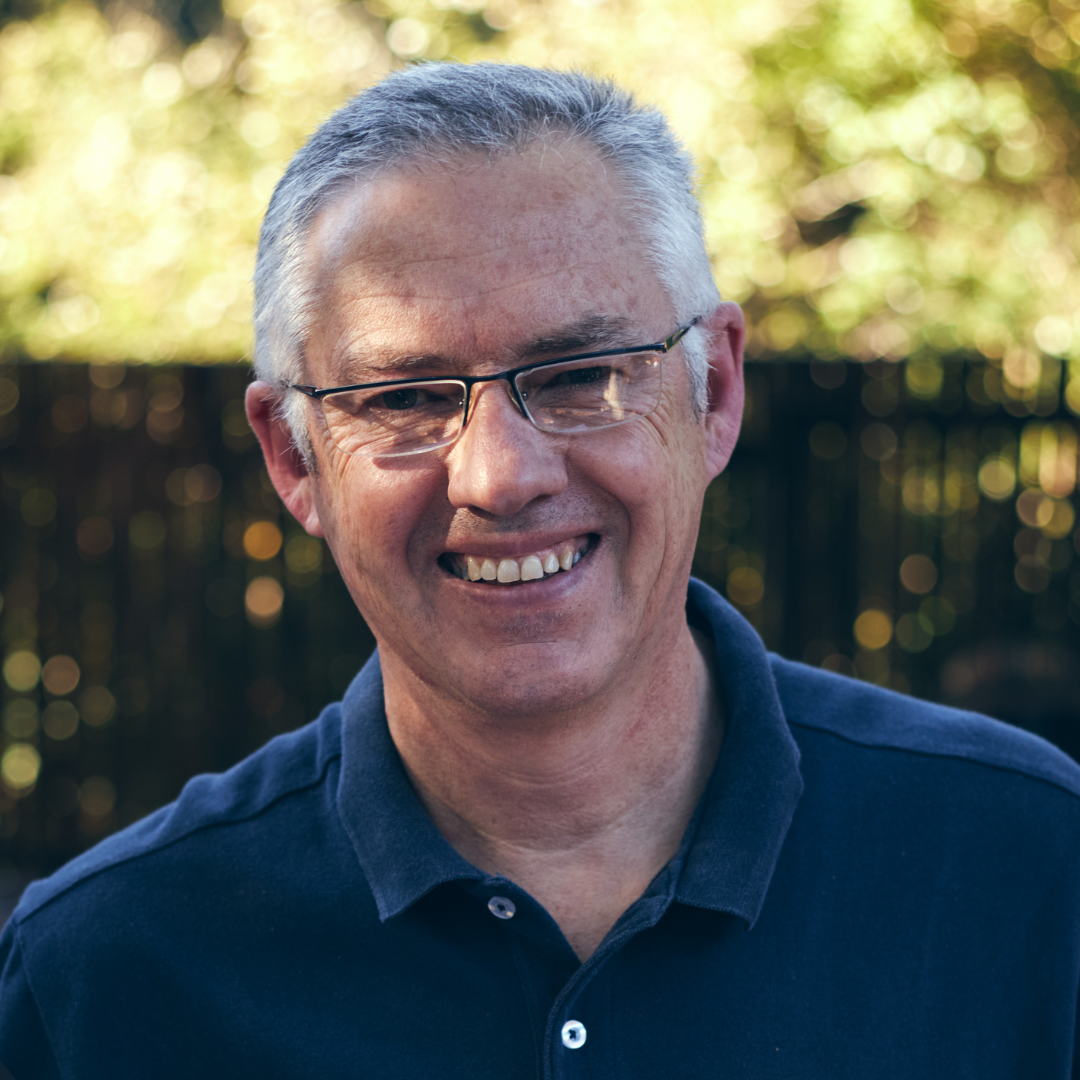 An older white man wearing a polo smiles for a photo.