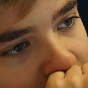 Close-up of a boy's face, with his hand on his chin and mouth in a thinking gesture.