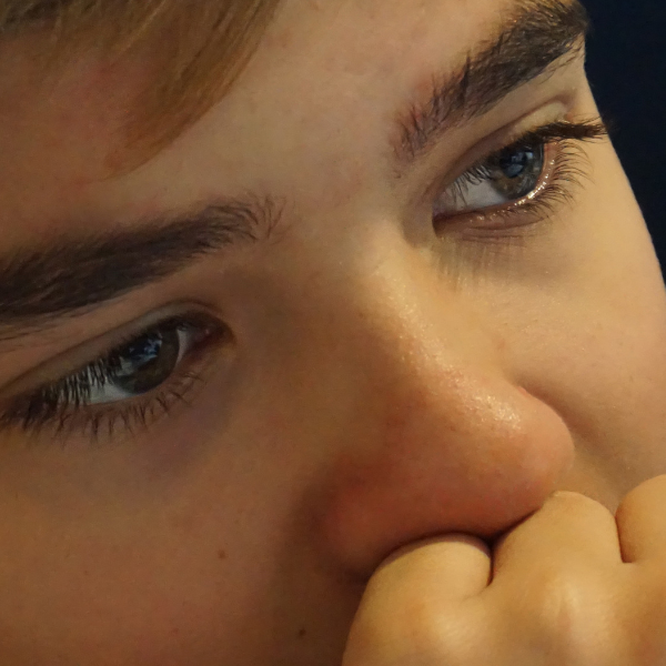 Close-up of a boy's face, with his hand on his chin and mouth in a thinking gesture.