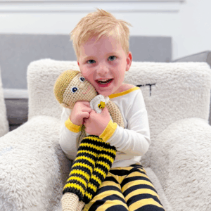 A young white boy sits in a fluffy chair, wearing bee stripe pants.