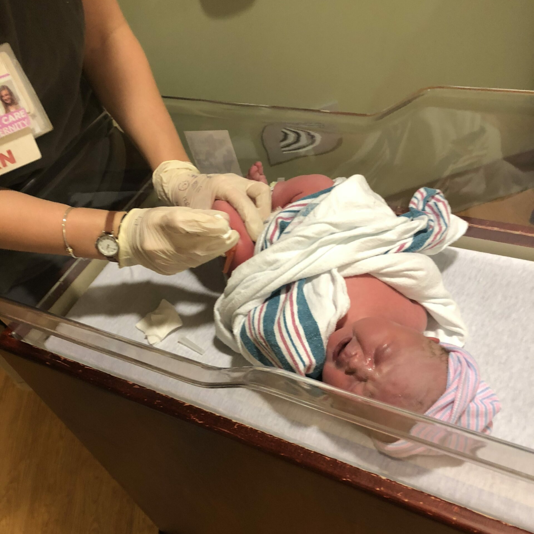 A newborn baby is given an injection in their leg by a nurse.