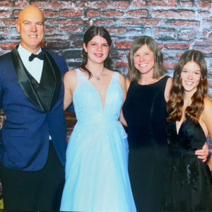 A family of four, formally dressed, poses in front of a brick wall.