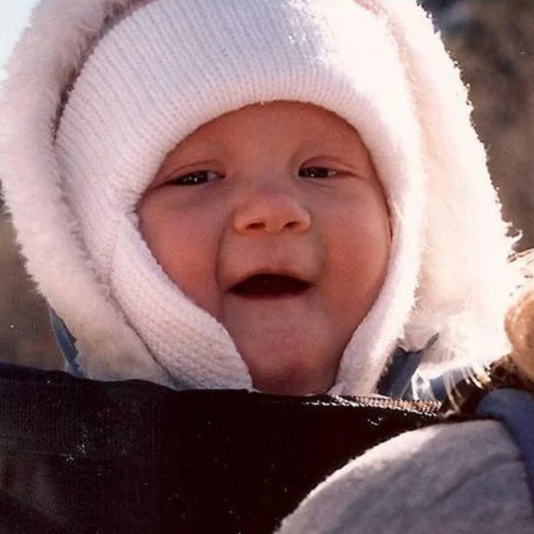 A baby in a wool winter hoodie and white knit cap.