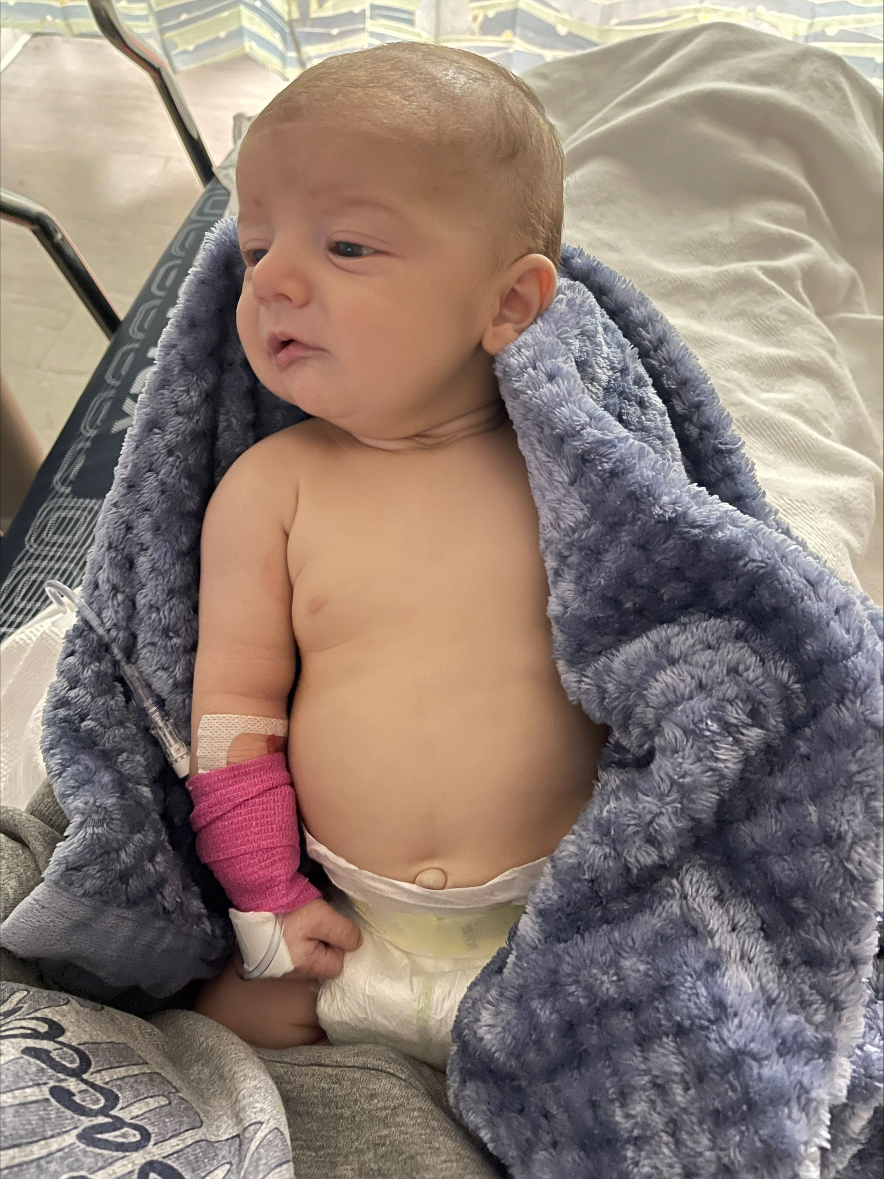 Baby Logan resting in a blue blanket at the ER, a pink wrap holding the IV in his arm