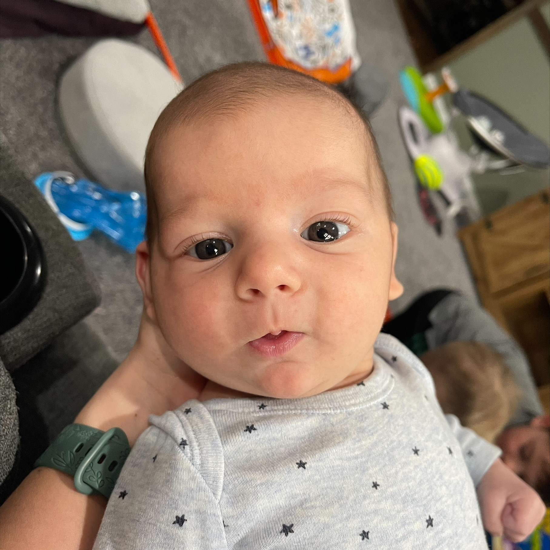 Baby Logan at seven weeks old in a gray star-print onesie, looking up at the camera