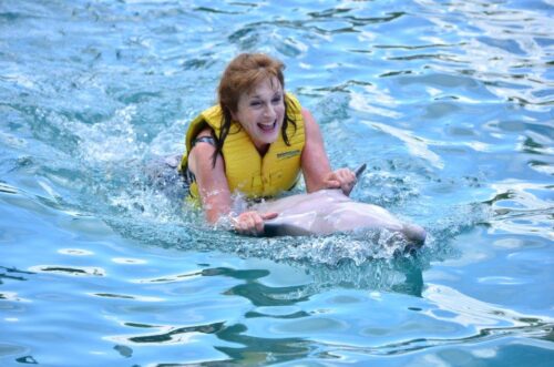 Marlene Moulder smiling in a yellow life jacket as she rides a dolphin in Cozumel