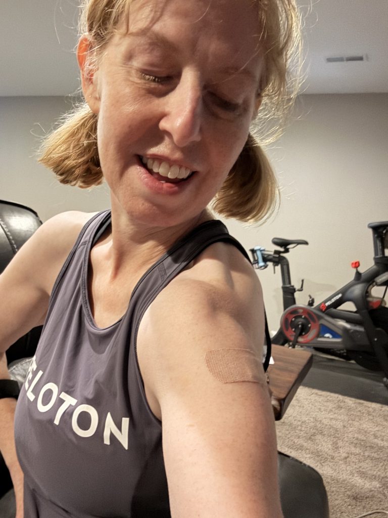 Woman in a workout tank taking a selfie in a home gym, bandage on her arm.